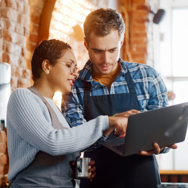 Two restaurant professionals look at information together on a laptop.